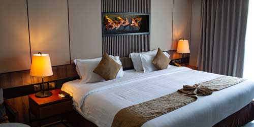 Image of a hotel room with bed, side tabels and lamps.